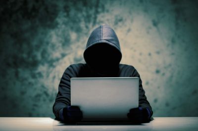 A person in a hoodie sitting at a table with a laptop, potentially involved in Amazon hijackers.