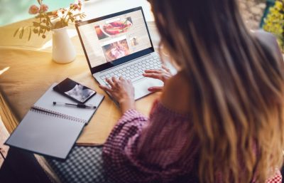 A woman using a laptop and a notebook to optimize Amazon product listings.